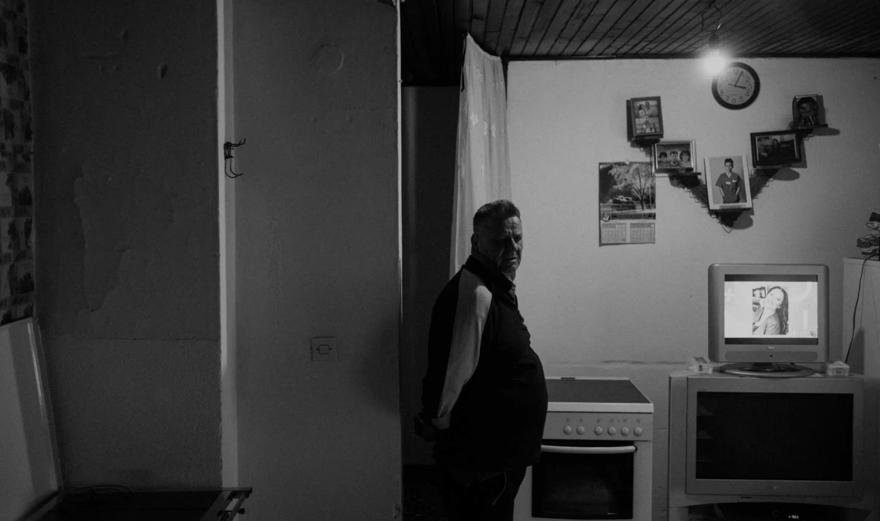 Zaim Alic stands in front of the TV in his barrack in the Ježevac refugee camp. Image by Jošt Franko. Bosnia and Herzegovina, undated.