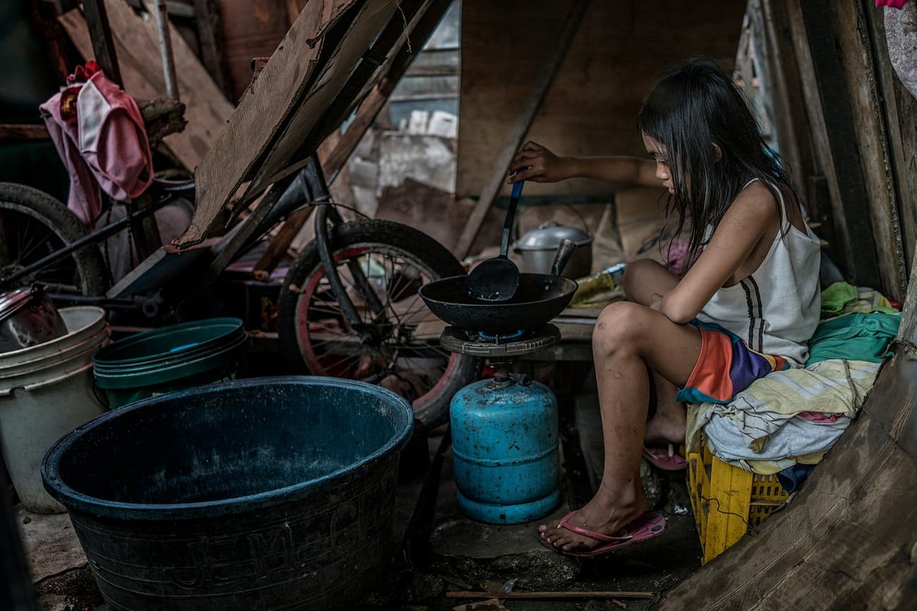 Lenie Banting’s other daughter, Rubylyn prepare an egg over a propane flame at their makeshift house on the former Smoky Mountain dumpsite. Image by James Whitlow Delano. Philippines, 2018. 