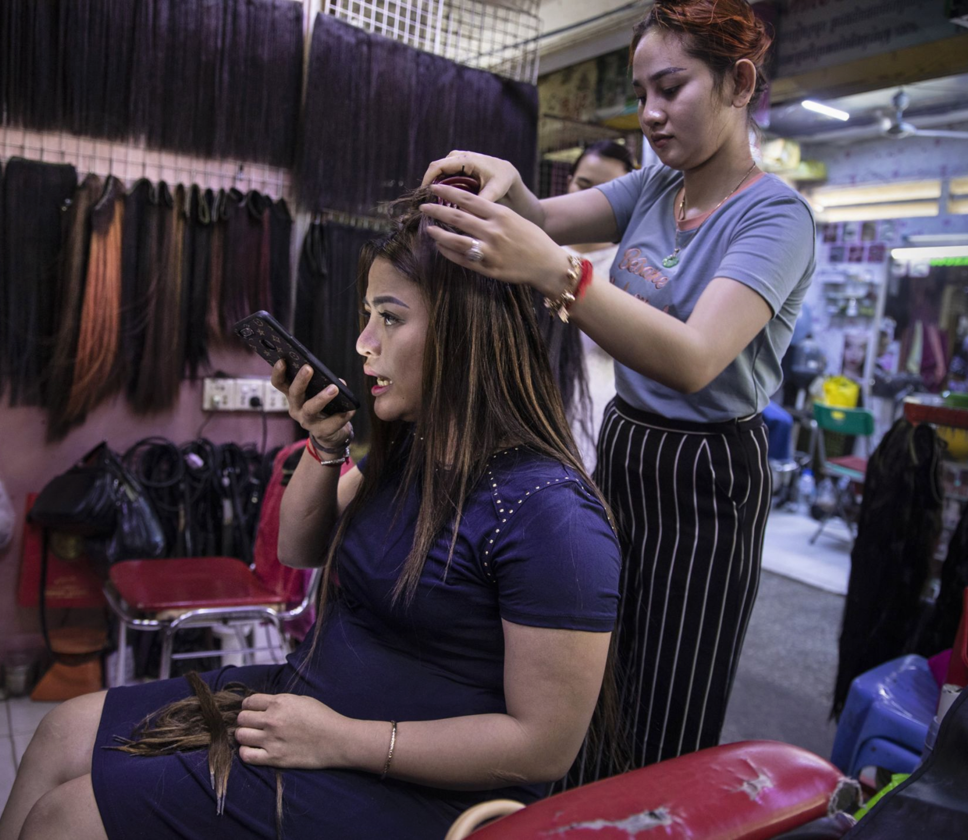 A hairdresser works on a customer at the Orussey shopping complex in Phnom Penh. Image by Paula Bronstein. Cambodia, 2019.