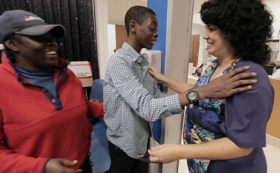 Djonsly Alcin (center), 14, and his mother Marie Belatrice Louis-Jean (left), 37, greet a Baptist Health nurse after arriving to get his weekly chemotherapy for a rare brain tumor. Image by José A. Iglesias. Haiti, 2018.