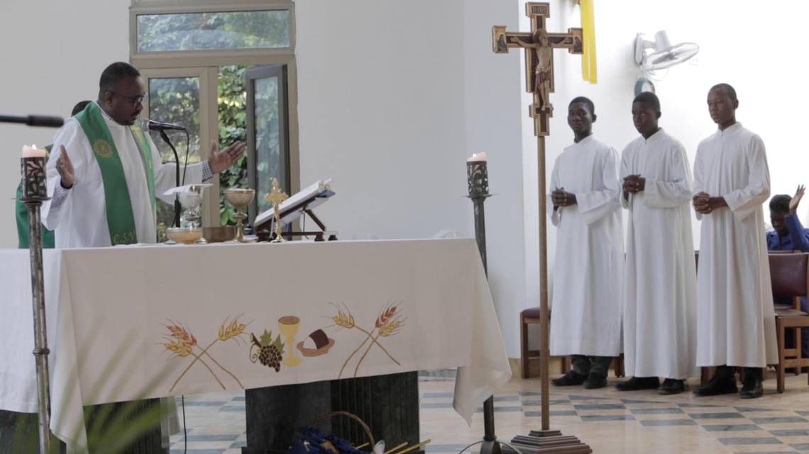 A deacon reads from the Scriptures as altar boys stand by during a Sunday service at the newly built St. Louis Roi de France in Turgeau, Haiti. Still in need of painting, the structure is functional, its priest said. Image by Jose A. Iglesias. Haiti, 2020.