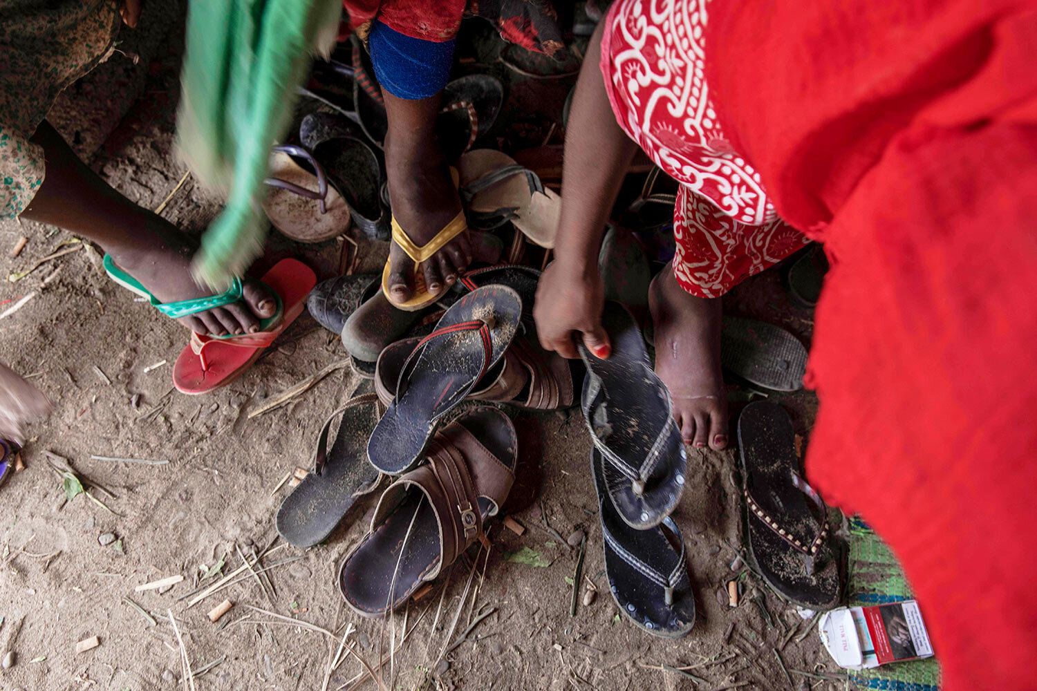 In this July 26, 2019 photo, Ethiopian migrant girls put on their slippers to go and eat outside their lockup known in Arabic as a "hosh," in Ras al-Ara, Lahj, Yemen. Some lockups hold as many as 50 women at a time. The women will stay here for several days until their transportation is ready. Image by Nariman El-Mofty / AP Photo. Yemen, 2019.
