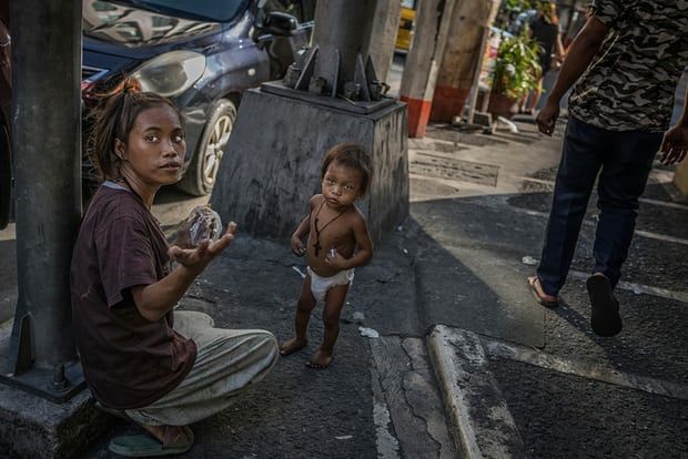 A homeless woman in Malate seeks change to buy food for her toddler. The streets of Manila are home to thousands of homeless Filipinos who sleep on the sidewalks, sea walls, under awnings and in stairwells - anywhere they can get rest without being told to move on. Image by James Whitlow Delano. Philippines, 2018. 