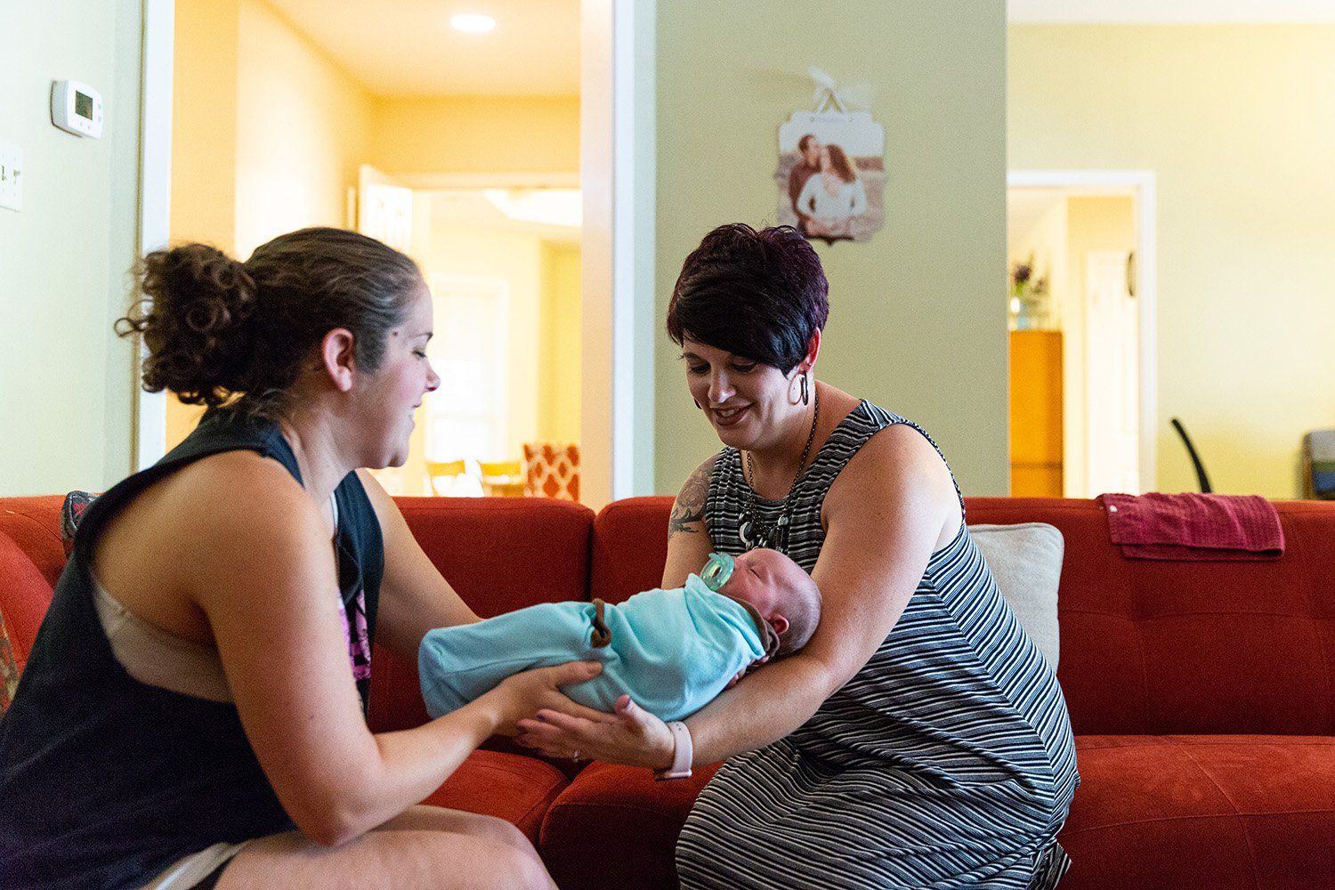 Hailey Frazier (left) gives her son Isaac to Sabrina Elliott (right), a doula in Abilene during a home visit. Image by Gary Rhodes for The Texas Tribune. United States, 2018. 