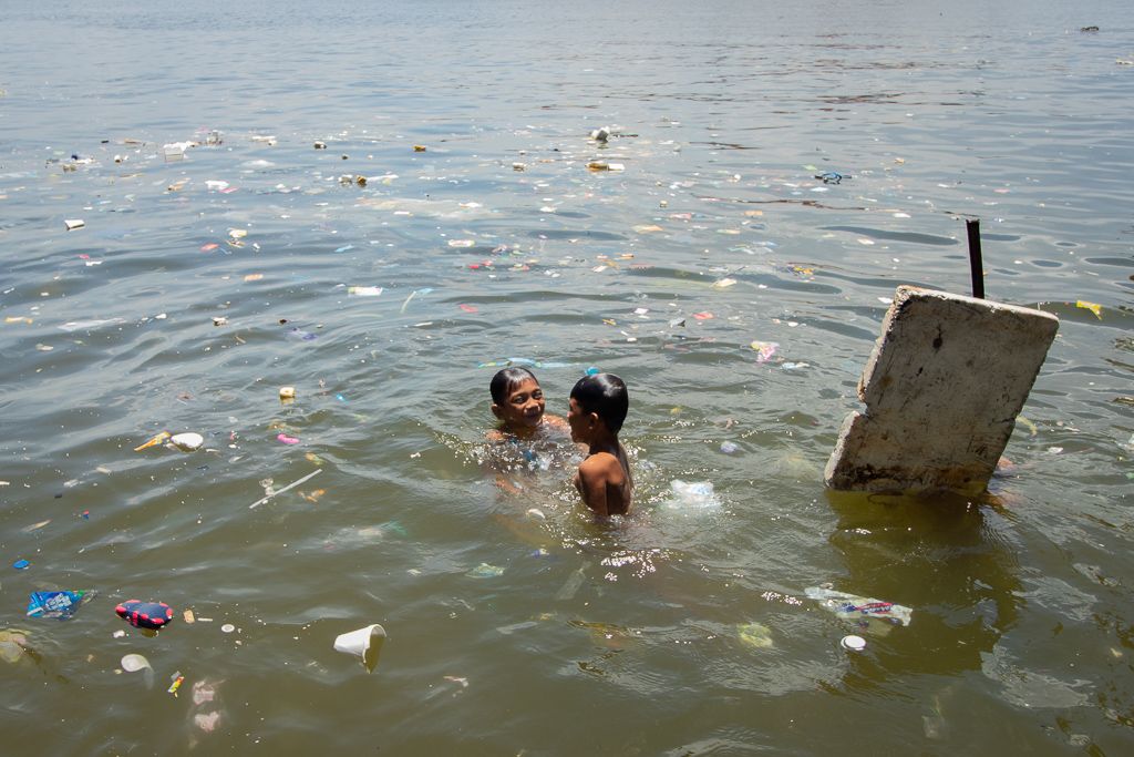 On a hot summer day, children swim in Manila Bay’s murky waters amid floating pieces of plastic and Styrofoam. Image by Micah Castelo. Philippines, 2019. 