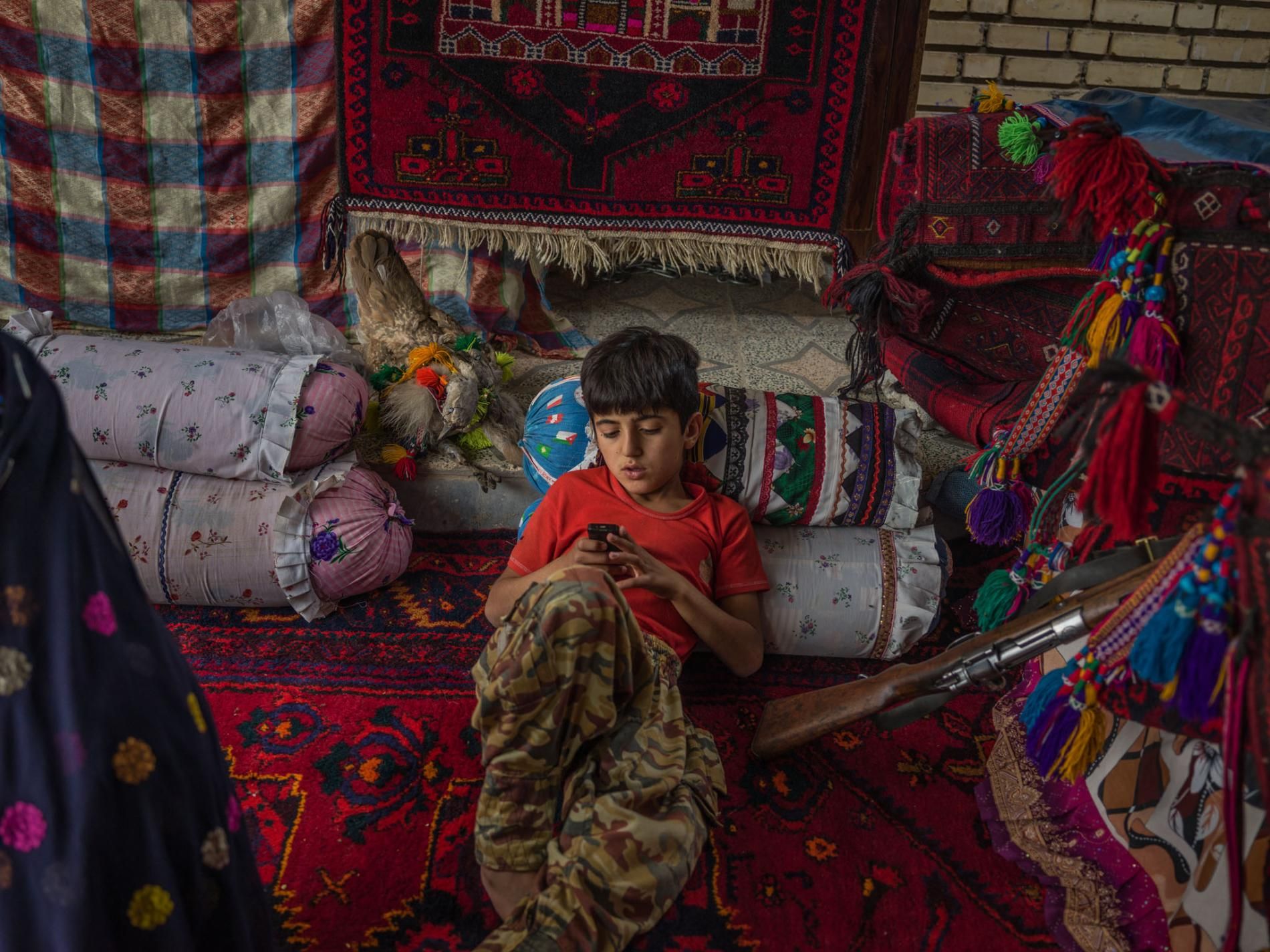 Mostafa Mokhtari, 10, sits in a tent in his grandparents’ yard. His grandparents decided to stay in a house to help their grandchildren attend school and study. But being accustomed to living in a tent, they made one for the yard. Image by Newsha Tavakolian. Iran, 2018.
