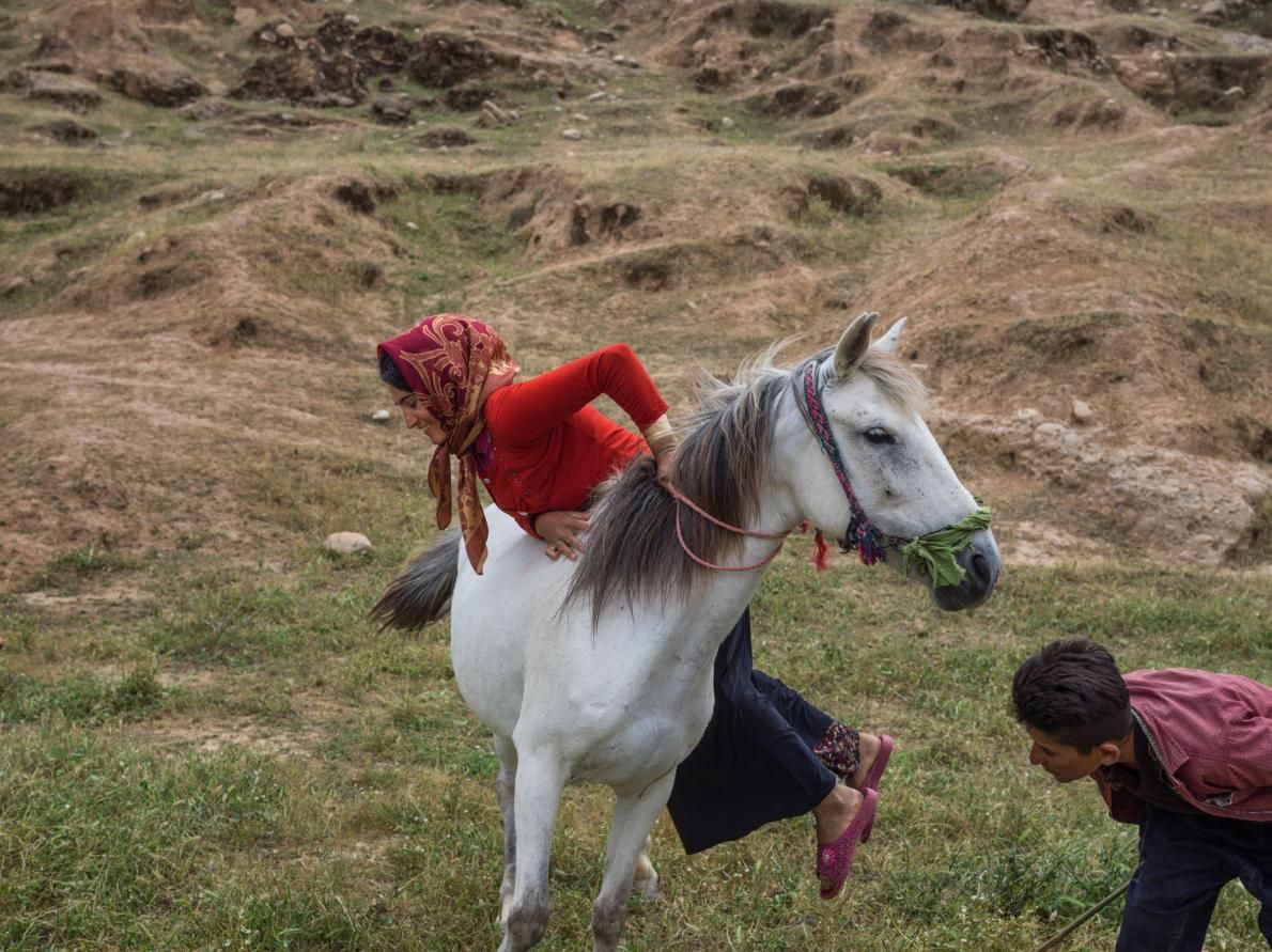 Parisa Zamani, 20, climbs onto her horse. She is considered an accomplished rider in her family. Many nomadic families have changed their lifestyles and settled in cities so girls may go to school. Image by Newsha Tavakolian. Iran, 2018.