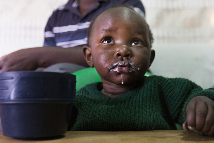 Elijah Muasya's 18-month old daughter, Nina, eats in her family's 400-square foot home in the Korogocho slum. The family has rare access to clean drinking water in their home for their family of four. Image by Mark Hoffman. Kenya, 2017. 