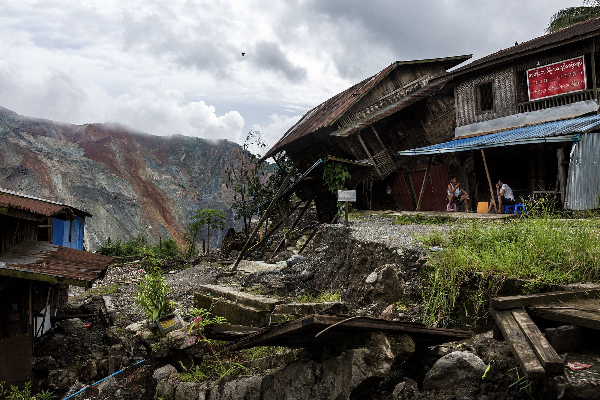 Residents sit near a damaged house caused by a landslide at a mining site in Hpakant in July. The landslide killed nearly 200 people. Image by Hkun Lat. Myanmar, 2020.