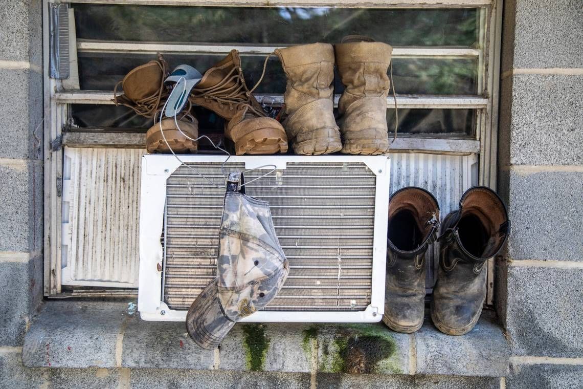 Boots and a hat dry on a window air conditioning unit at a Johnston County farmworker camp on Thursday, August 27, 2020. Air conditioning is considered a luxury by many farmworkers in North Carolina farmworker camps. Image by Travis Long. United States, 2020.