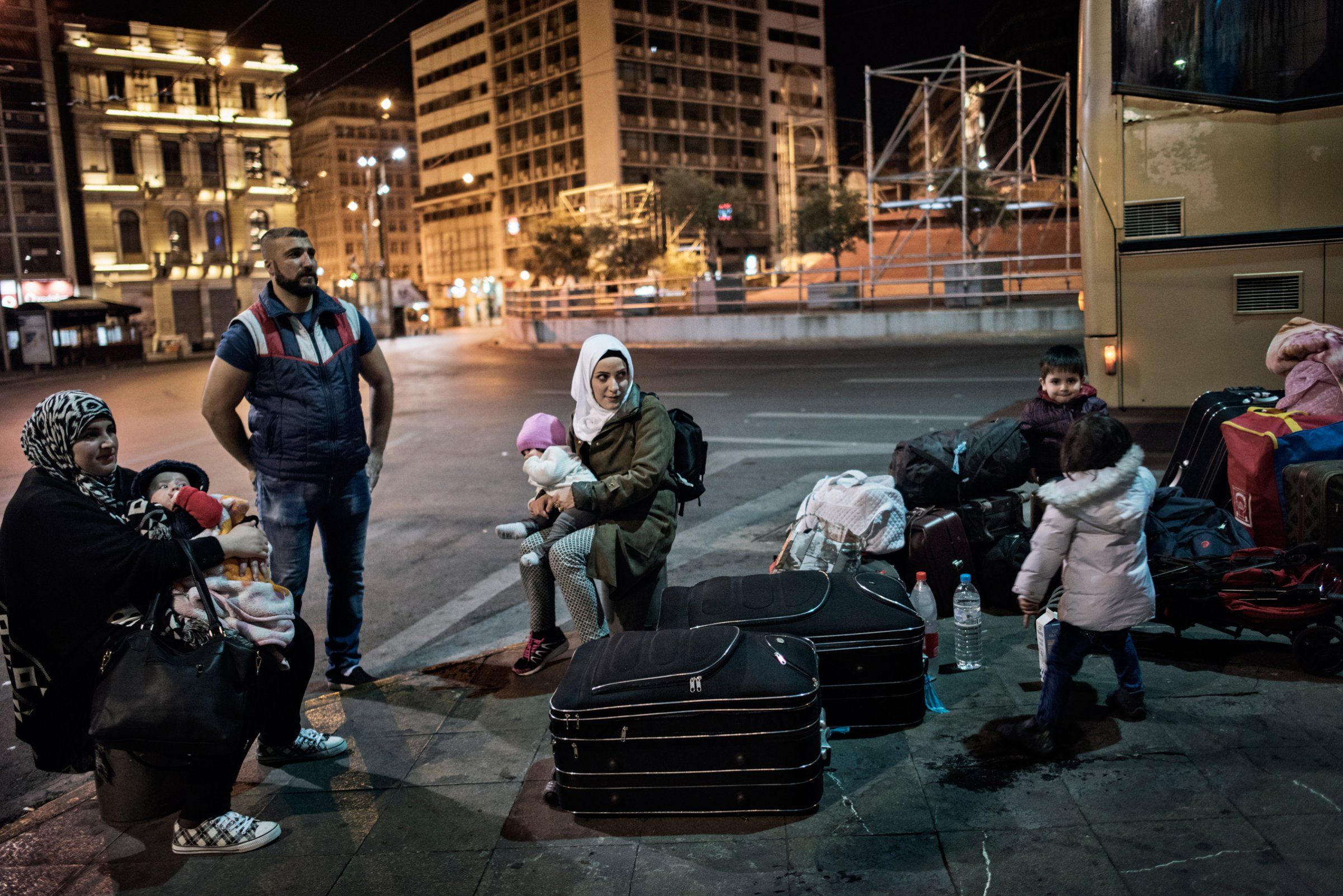 Syrian refugee Taimaa Abzali and her husband Muhanned Abzali, and their six month old daughter, Heln, and son Wael, wait in Athen's Ommonia square for transfer to the airport alongside Muhanned's brother Mufeed, his wife, Iman, and their two children, from Athens to Estonia for relocation. Image by Lynsey Addario. Greece, 2017. 