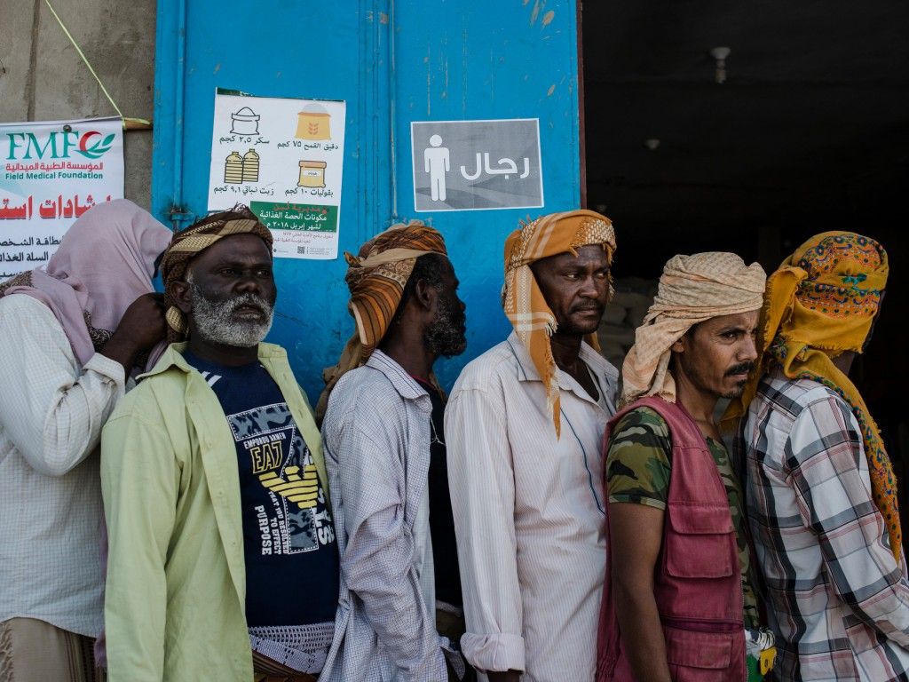 Yemeni men stand in line waiting for a weekly food distribution in Fayoush. Image by Alex Potter. Yemen, 2018. 