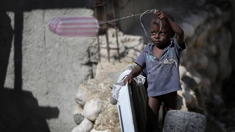 A young child uses a plastic bag as a kite at Teren Toto camp. Ten years after Haiti’s 2010 earthquake, the camp is among 22 official camps where homeless quake survivors still live. Image by Jose A. Iglesias. Haiti, 2019.