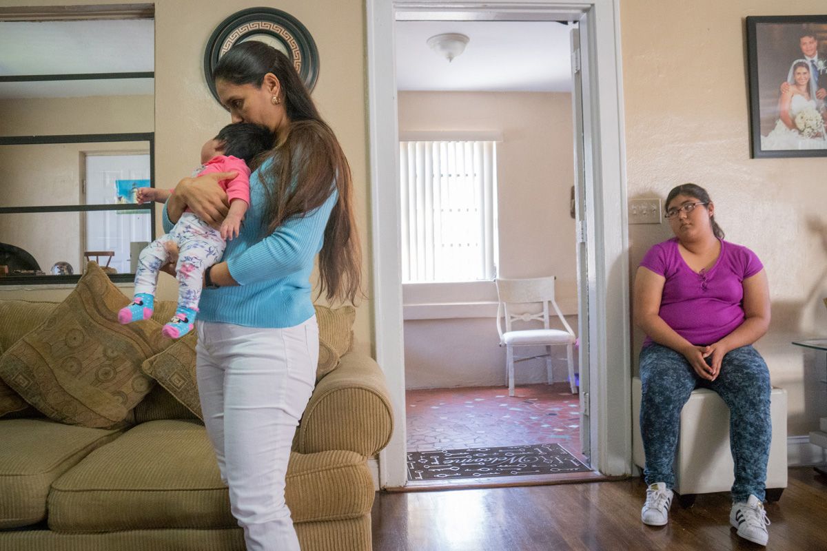 Yessica Flores, 38, holds her daughter Daniella Elizabeth Yac as Andrea Flores, 14, Daniella's sister, looks on. Image by Roy Llera. United States, 2017.