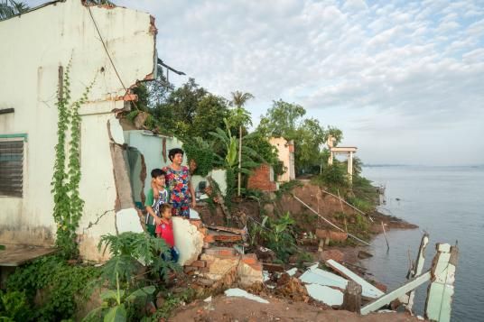 Ha Thi Be and her two grandsons stand in the ruins of her ancestral home along the Tien River in Dong Thap Province. The government warned her to relocate inland to live with her son in January 2017, two months before the house eventually collapsed. "But everything I own was in this house, and now everything is gone," she said. Image by Sim Chi Yin. Vietnam, 2017.