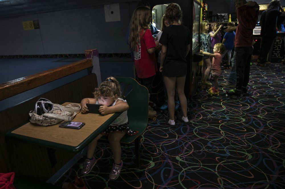 A girl is immersed in a smartphone game while others play in an arcade at a skating rink in Anna, Ill. Image by Wong Maye-E/AP Photo. United States, 2020.