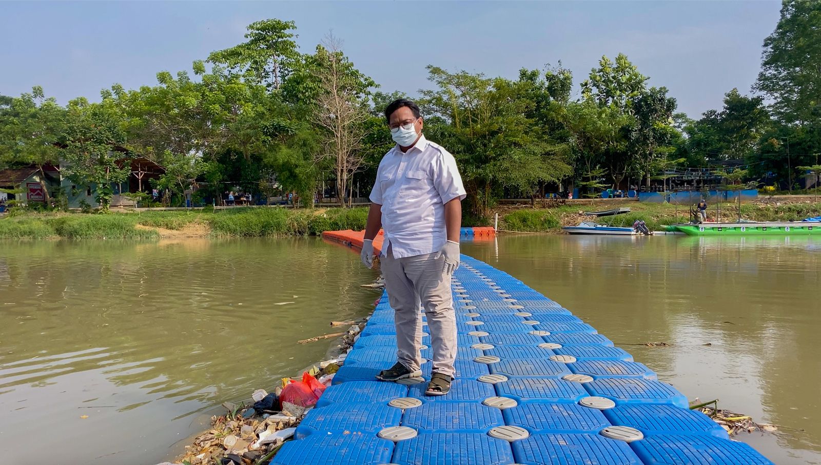 Ade Yunus, founder of environmental organisation Bank Sampah Sungai Cisadane (Cisadane River Waste Bank) or Banksasuci, stands on a floating boom used to collect waste from the Cisadane River in Tangerang, Indonesia. Image by Adi Renaldi. Indonesia, undated.