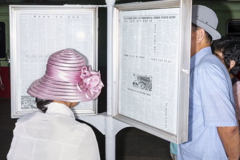 Commuters reading the official newspaper on a Pyongyang Metro platform.