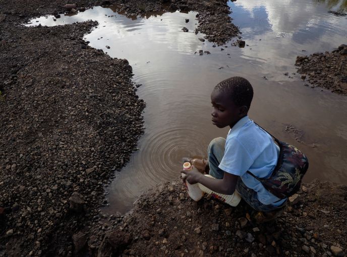 Brian Jovo, 14, collects water from a pool of water. Jovo and other children help older siblings and adults at the Black Mountain. Image by Larry C. Price. Zambia, 2017.