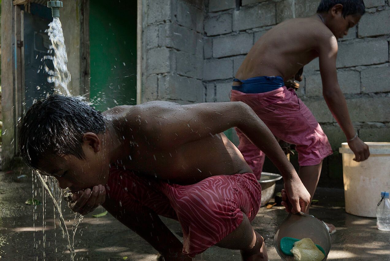 Children kneel under a spigot to bathe in the Koronadal City sanctuary. Image by Chien-Chi Chang/Magnum Photos. Philippines, 2018.