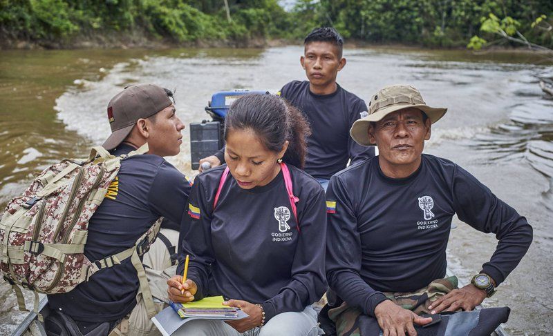 Four members of the G.I.A. sit in a boat during a routine tour of the Amacayacu River. A woman in the foreground takes notes on a yellow notepad. 