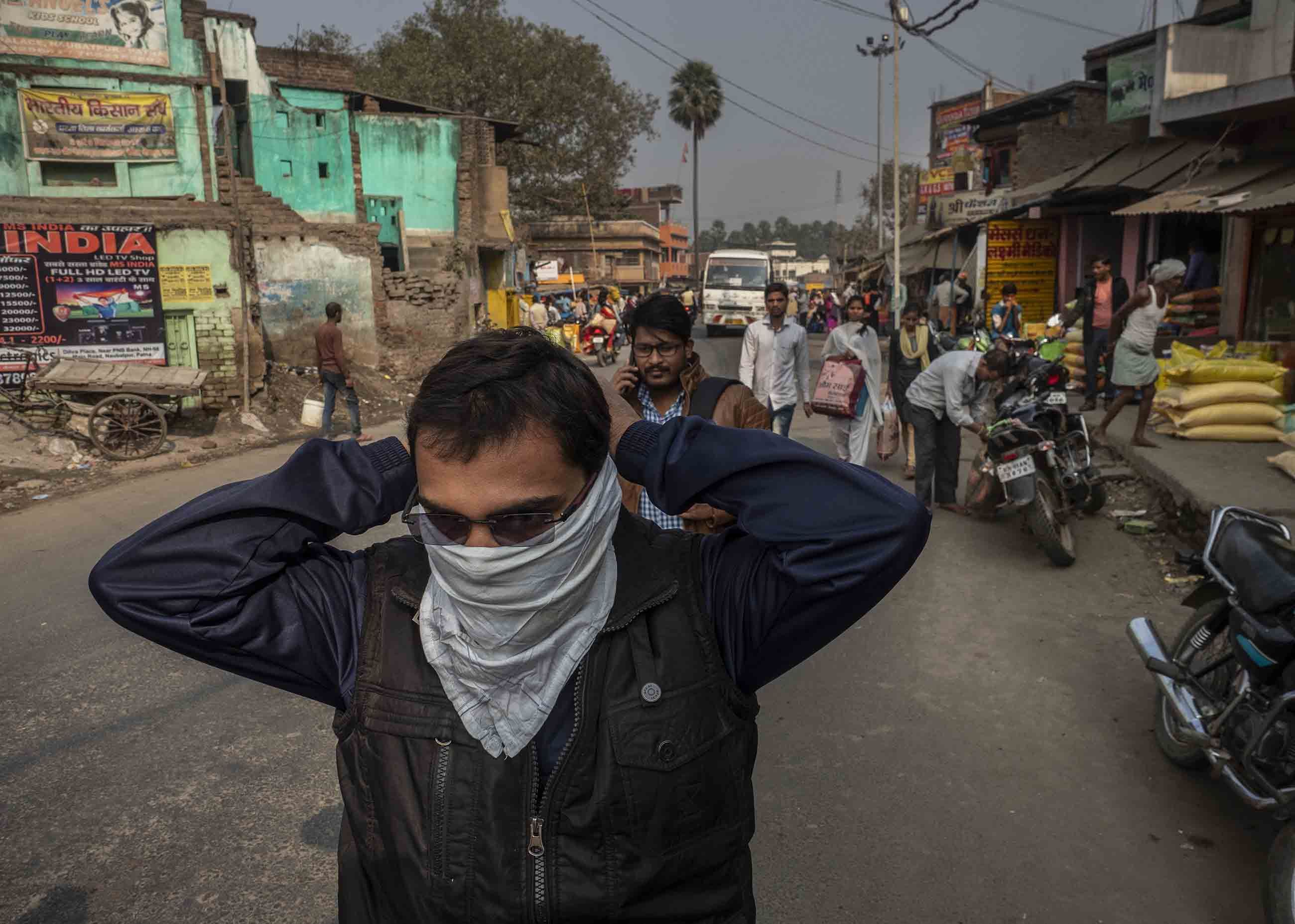 The open burning of trash  adds to the daily cloud. Here, a man ties a scarf over his face after encountering a smoldering pile of trash. Image by Larry C. Price. India, 2018.