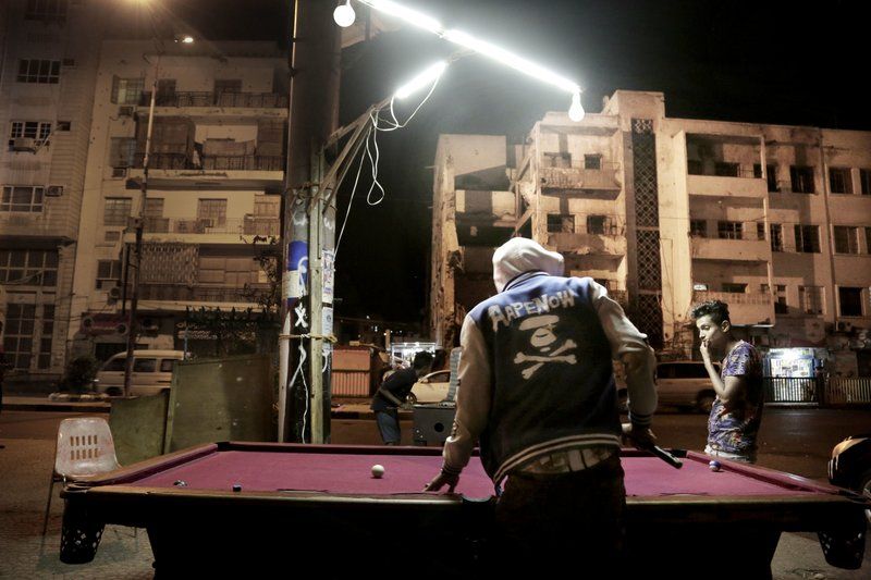 Youth play pool on a street in front of damaged buildings due to the war. Image by Nariman El-Mofty. Yemen, 2018. 