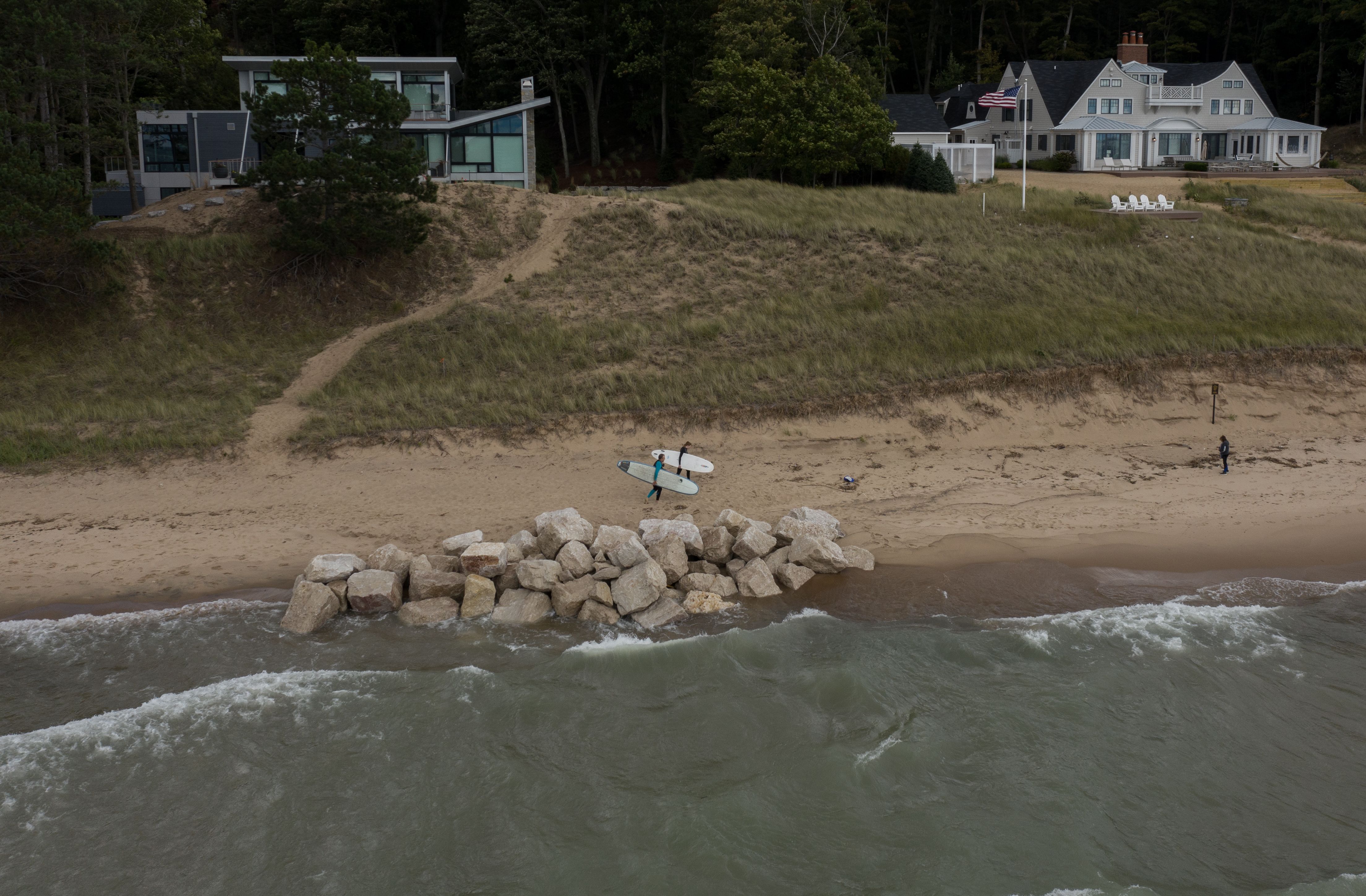 Surfers Michael Christensen, left, and daughter Julia walk near a pile of boulders used for construction of a seawall in front of a new house near Oval Beach in Saugatuck, Michigan, on Sept. 29, 2020. Image by Zbigniew Bzdak/Chicago Tribune. United States, 2020.