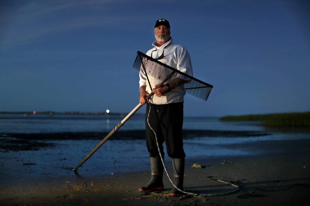 Erick Scherer made his living at night, using a custom-made, sharp-tined steel rake to rake up the shallows at low tide for silver fish called sand lances. Image by John Tlumacki. United States, 2019.