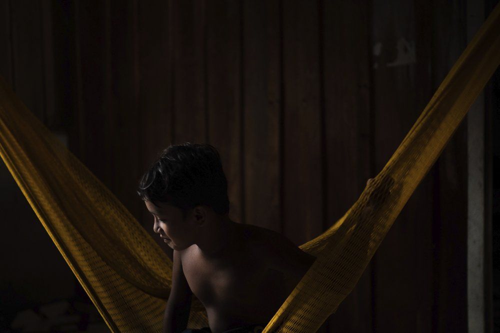 A youth from the Sateré Mawé indigenous ethnic group sits in a hammock in the Gaviao community near Manaus, Brazil, Friday, May 29, 2020. In the midst of the new coronavirus pandemic, Brazil's indigenous people have neither the protective isolation of their homelands nor the government care that drew many to the city of Manaus in the first place. Image by Felipe Dana / AP Photo. Brazil, 2020.