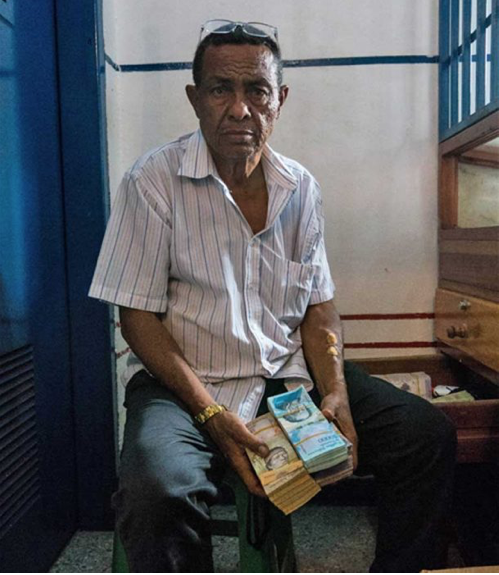 The owner of a local gold pawn shop in Tumeremo, Bolivar state, shows a stack of Venezuelan money, worth only a few dollars due to the nation’s rapidly escalating inflation. Image by Bram Ebus. Venezuela, 2017.
