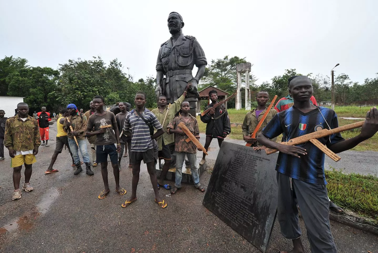Ex-Seleka rebels with wooden weapons stand next to a statue of Emperor Bokassa at his Berengo palace in 2014. Image by Sia Kambou. Central African Republic, 2014. 