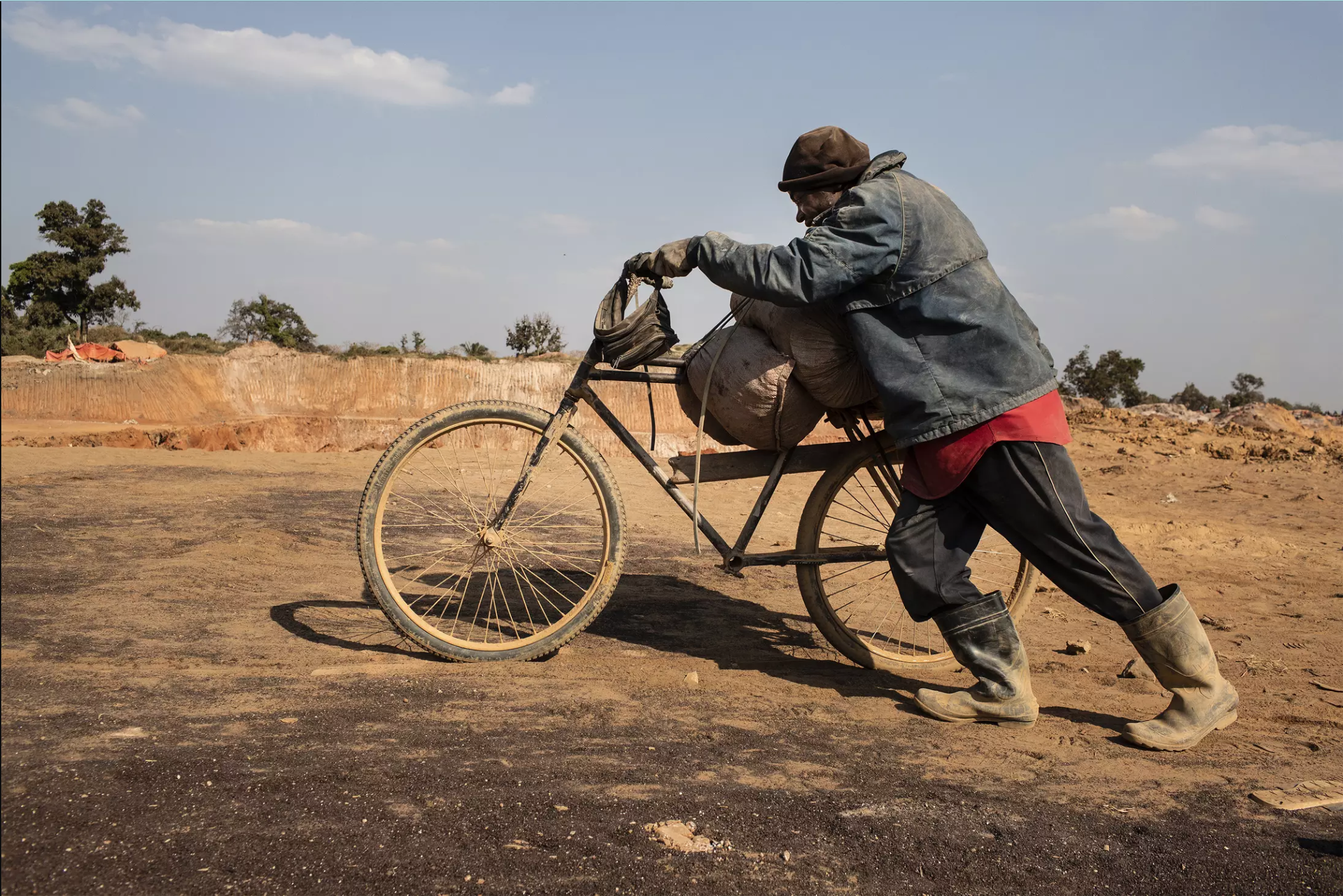 A miner pushes a bicycle without pedals piled with sacks of cobalt from a mining pit to the depot inside the Kasulo mine. Image by Sebastian Meyer. Democratic Republic of Congo, 2018.
