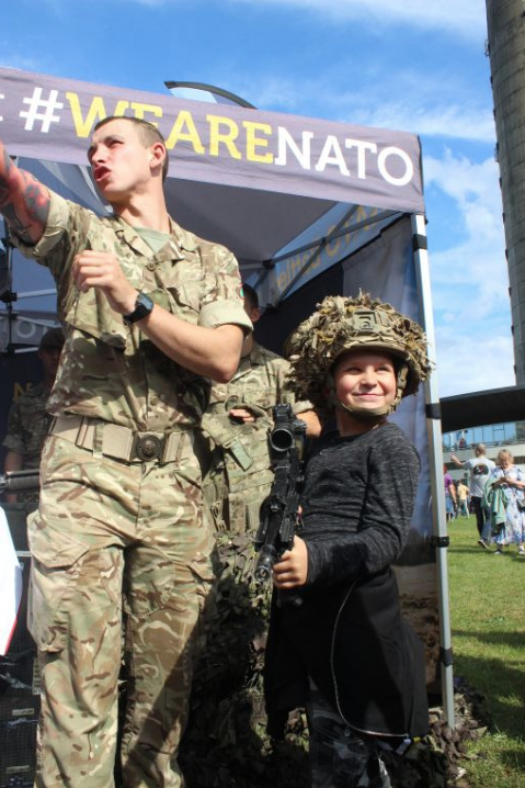An Estonian child wears a helmet and carries a British gun provided by British NATO EFP Troops showcasing their capabilities in Tallinn on the Restoration Day in Estonia. Image by Hani Zaitoun. Estonia, 2019.