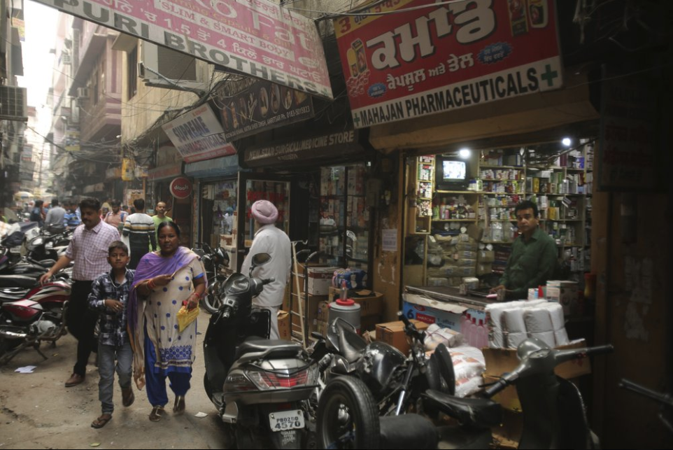 In this Oct. 30, 2019, photo, people walk past drugstores where tramadol was once easily accessible in Amritsar, in the northern Indian state of Punjab. The pills were everywhere, as legitimate medication sold in pharmacies, but also illicit counterfeits hawked by itinerant peddlers and street vendors. India has twice the global average of illicit opiate consumption. Researchers estimate about 4 million Indians use heroin or other opioids, and a quarter of them live in the Punjab, India's agricultural heartland bordering Pakistan. Image by Channi Anand / AP Photo. India, 2019.