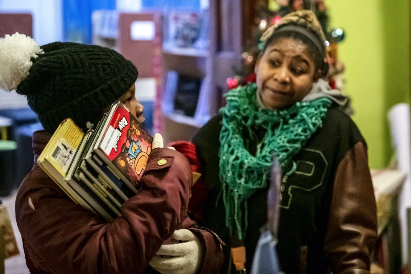 Kee’Miyah holds a stack of books that she plans on checking out to read over the weekend as Glaze speaks to her about making sure she does her chores before reading. Image by Michael M. Santiago/Post-Gazette. United States, 2019.