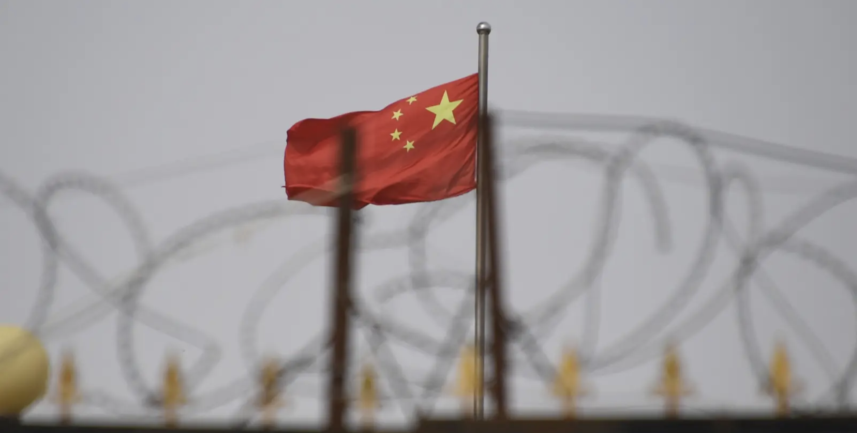 The Chinese flag is seen behind razor wire at a housing compound in Yangisar, south of Kashgar, in China's western Xinjiang region, June 4, 2019. Image by Greg Baker/Getty Images. China, 2019.