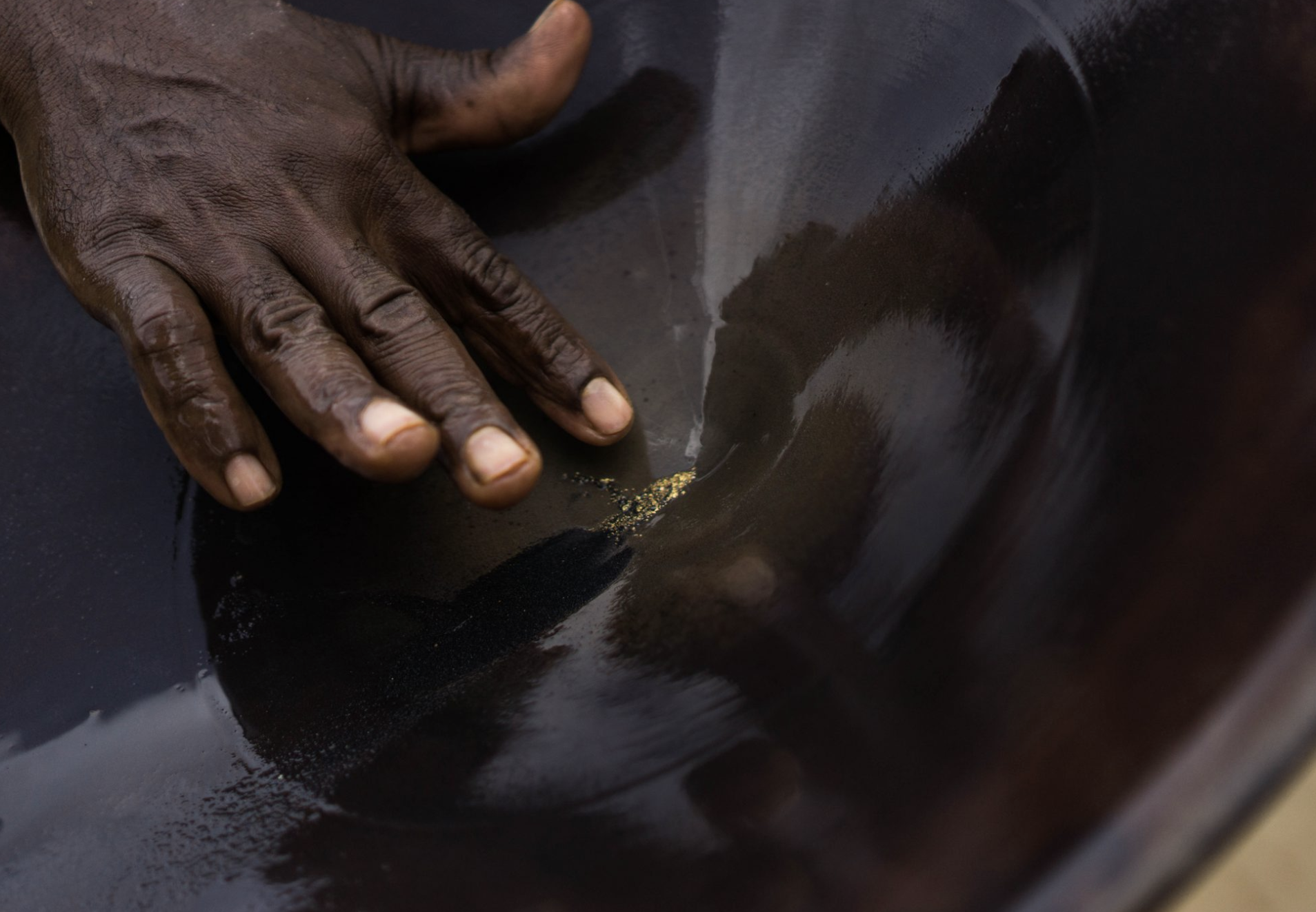 A miner points to the gold left behind after the gold-bearing black sand and gravel was spun in a battel. Image by Bram Ebus. Guyana, undated.