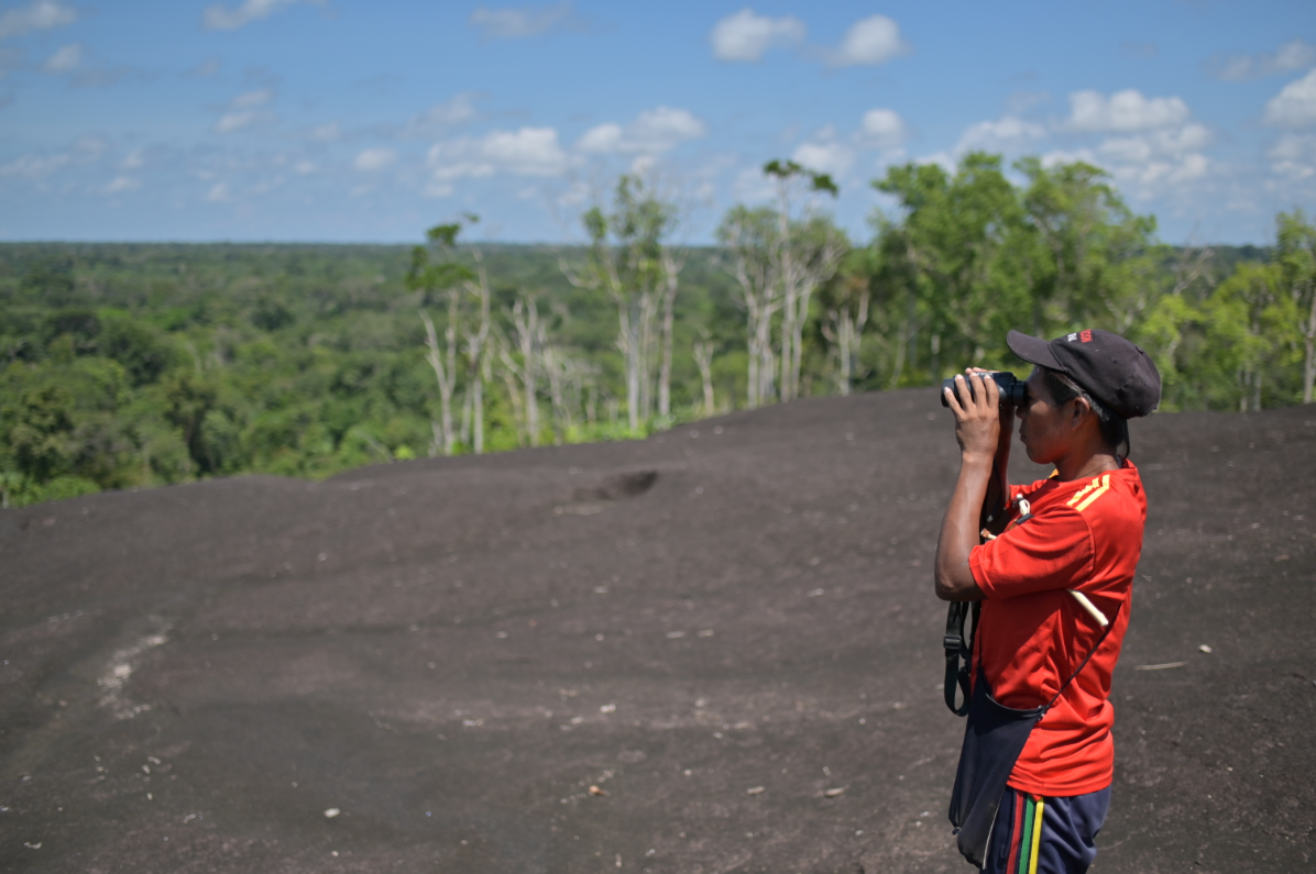 An indigenous man watches the jungle and other hills with the help of a pair of binoculars. Image by Luis Ángel. Colombia, undated.