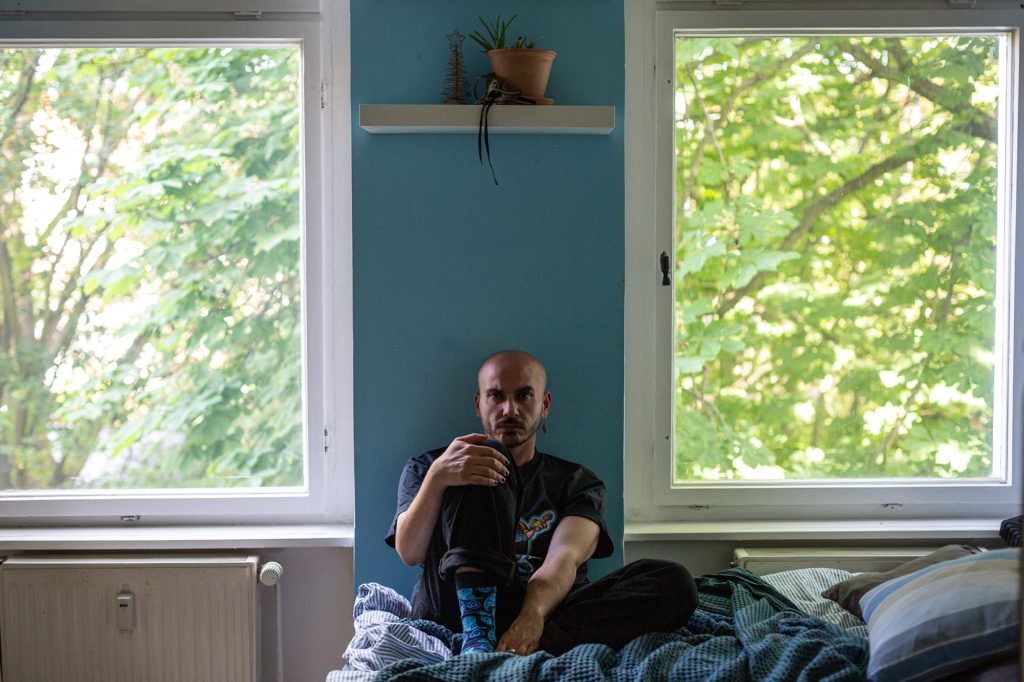 Hamoudi sits on his bed in his Berlin flat. Originally from the Syrian city of Raqqa, Hamoudi actively protested against the Syrian regime and ISIS and was arrested and tortured multiple times. Image by Bradley Secker. Germany, 2020.