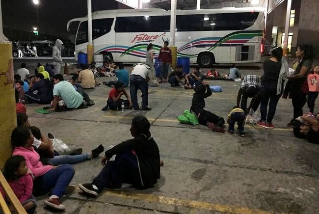 Chartered buses are parked behind a group of migrants at an immigration checkpoint in Nuevo Laredo. The buses are scheduled to transport the group to the state of Chiapas, near the Guatemalan border. Aug. 7, 2019. Image by Daniel Méndez. Mexico, 2019.