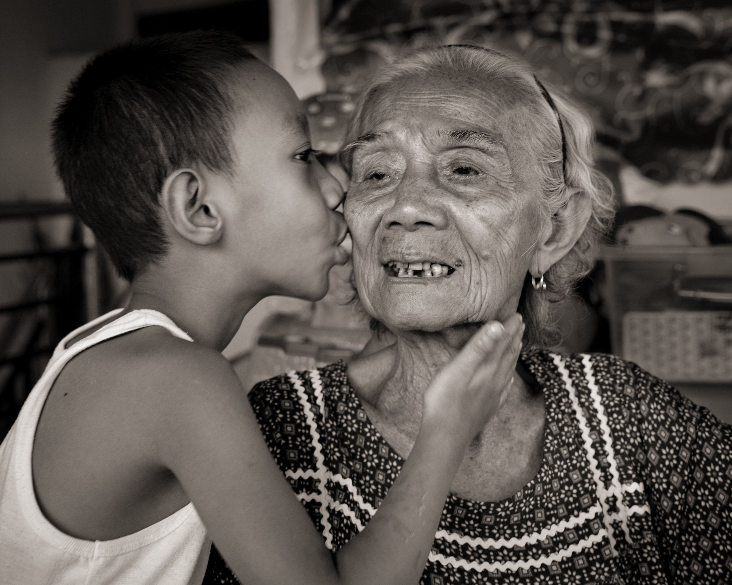 Narcisa Claveria receives a gentle kiss from her great-grandson, Joseph Tena, 8, whom she and her husband have raised since his father died when he was an infant. Claveria was 12 when Japanese soldiers took her as a sex slave for 1 1/2 years. They raped her mother and skinned her father alive before burning down their house. She could hear him scream, "Children, where are you? I'm in such pain." Image by Cheryl Diaz Meyer. Philippines, 2019.
