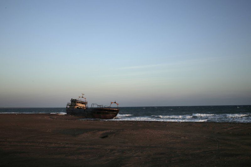 This Feb. 10, 2018, photo shows a shipwreck abandoned on the shore from Mocha to Aden in Yemen. On the beach, old pleasure venues also lie empty, broken and deserted due to the civil war here. A shattered night club and a vacant children’s theme park are ghostlike reminders of generations past. Image by Nariman El-Mofty. Yemen, 2018. 


