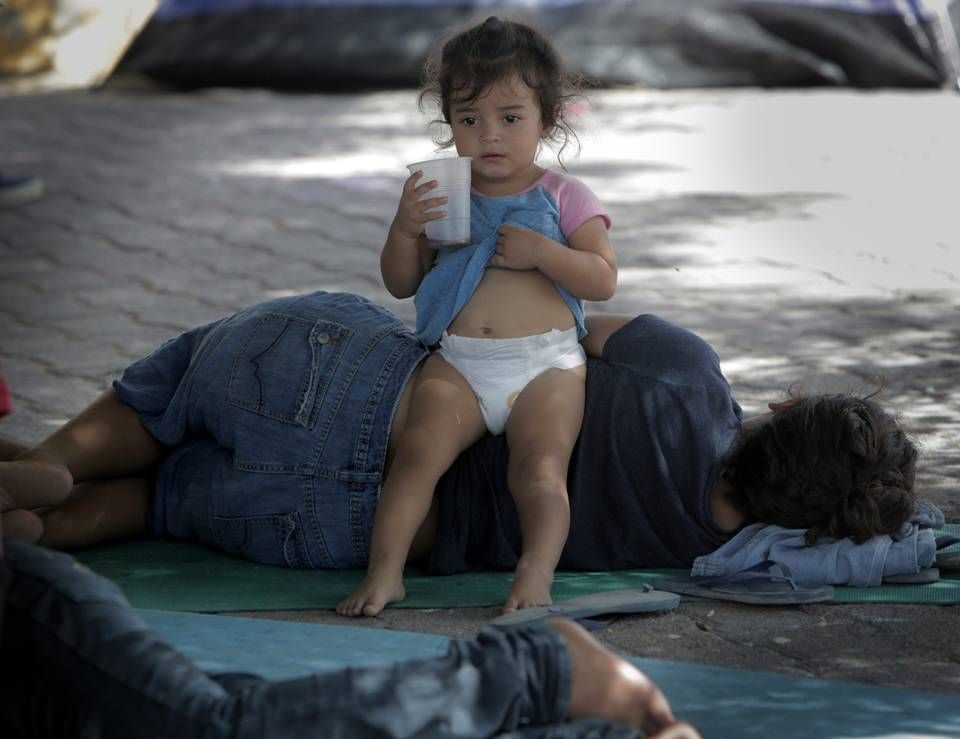 A child sits on her mother in the shade of a tree in a migrant camp next to the Gateway International Bridge in Matamoros, Mexico. Migrants who have some money usually rent a room to wait out the time it takes to get asylum in the United States. Those who don’t usually stay in the small camp by the bridge. Image by Jose A. Iglesias. Mexico, 2019.