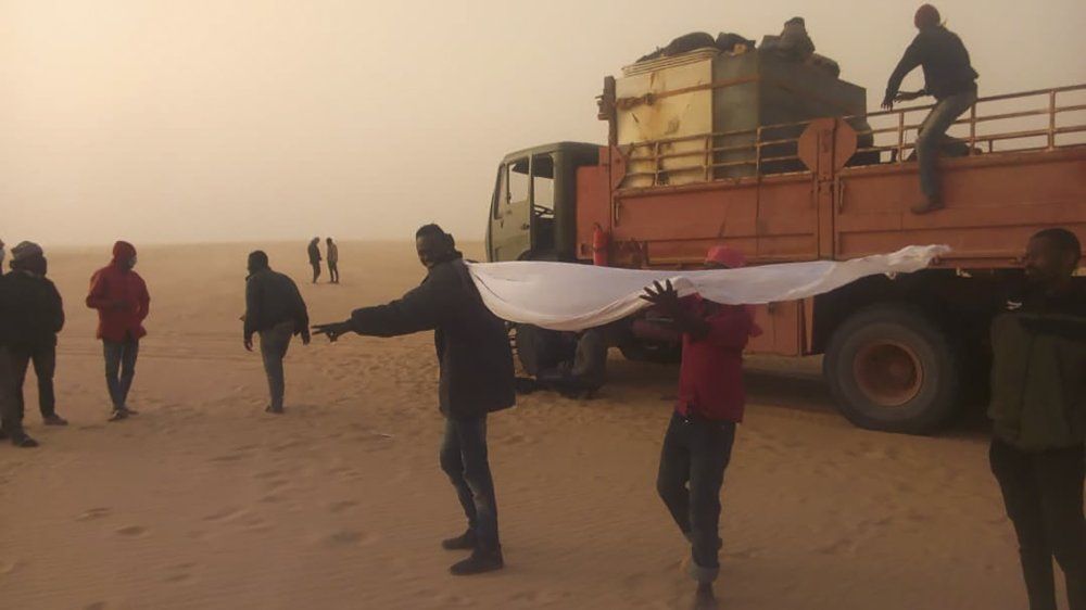 This March 22, 2020 provided by migrant Tayeb Saleh, shows fellow migrants standing in the sand while they await help getting out in the Libyan Sahara near the border with Sudan. (Tayeb Saleh via AP)