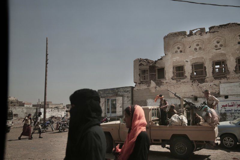 In this Feb. 12, 2018, photo, women walk past Saudi-led coalition backed forces, who are leading the campaign to take over Hodeida, as they patrol Mocha, a port city on the Red Sea coast of Yemen. Violence, famine and disease have ravished the country of some 28 million, which was already the Arab world’s poorest before the conflict began. The conflict pits a U.S.-backed, Saudi-led coalition supporting the internationally recognized government, which has nominally relocated to Aden but largely lives in exile, against rebels known as Houthis. Image by Nariman El-Mofty. Yemen, 2018. 

