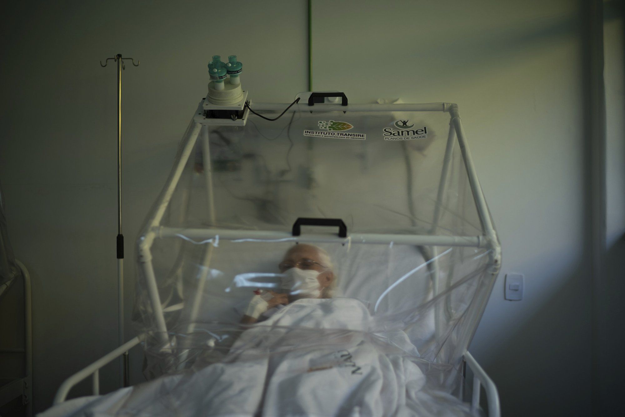 An elderly COVID-19 patient is treated inside a non-invasive ventilation system named the Vanessa Capsule at a municipal field hospital Gilberto Novaes in Manaus, Brazil, Monday, May 18, 2020. Image by Felipe Dana / AP Photo. Brazil, 2020.