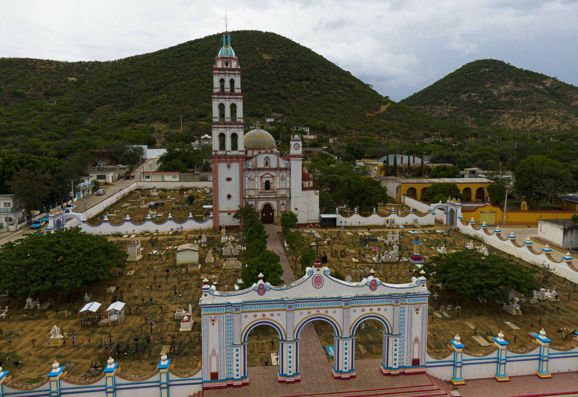 Graves surround the church of San Jeronimo Xayacatlan, Mexico, a town from which nearly a third of residents have emigrated to New York, Friday, June 26, 2020. Most departed in the 1990s or the first decade of the 21st century, leaving behind farm work to cross illegally into the United States. Image by Fernando Llano/AP Photo. Mexico, 2020.
