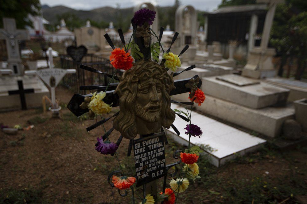 A sculpture of Jesus stands as a headstone at the cemetery in San Jeronimo Xayacatlan, a town in Mexico from where nearly a third have emigrated to New York, Thursday, June 25, 2020. On April 17, the church bells tolled for the first COVID-19 victim from the town, a young man living in New York. Four days later, another died. Image by Fernando Llano/AP Photo. Mexico, 2020.