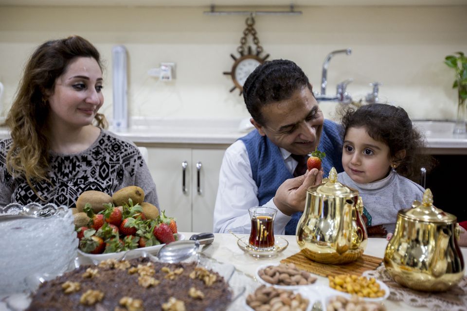 Dr. Faris offers his granddaughter, Elena Faris, 3, a strawberry after dinner with his daughter, Dr. Jumana Mohammed, left, and the rest of his family at his home in Erbil, Iraqi-Kurdistan on Feb. 5, 2019. Image by Brontë Wittpenn. Iraq, 2019.